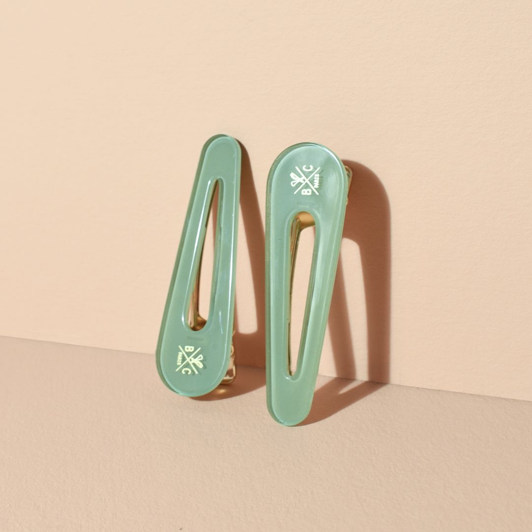 Lot de deux barrettes plates Bachca en acétate vert d’eau avec fermoir doré, design épuré et raffiné, posées sur fond beige rosé.