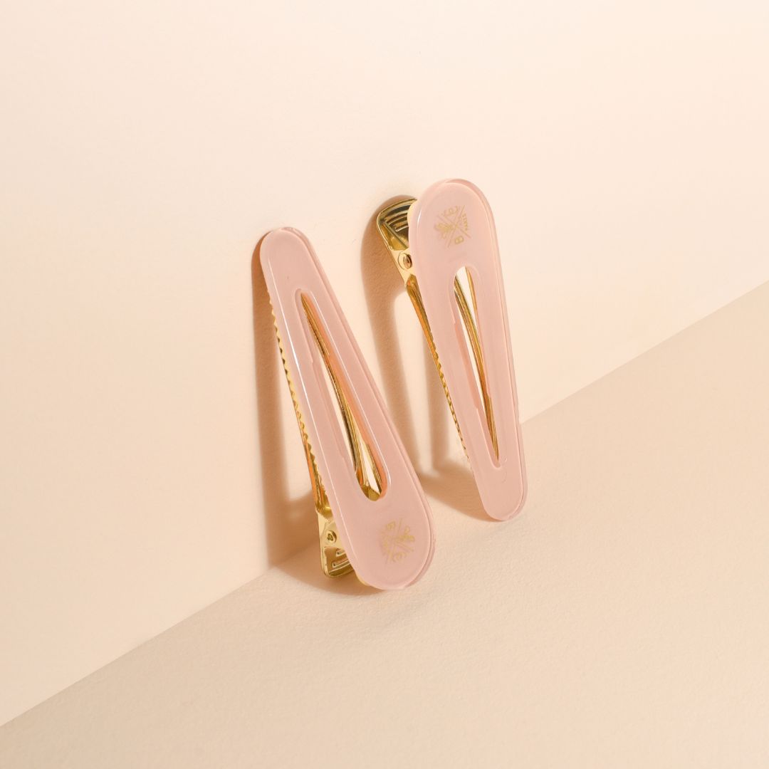 Lot de deux barrettes plates Bachca en acétate rose dragée avec finition dorée, design minimaliste et élégant, posées sur fond beige.