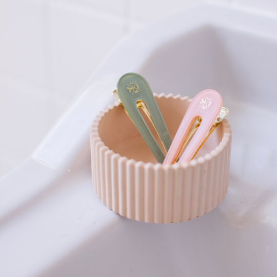 Duo de barrettes Bachca en acétate vert d’eau et rose dragée, posées dans un pot beige, accessoires cheveux élégants.