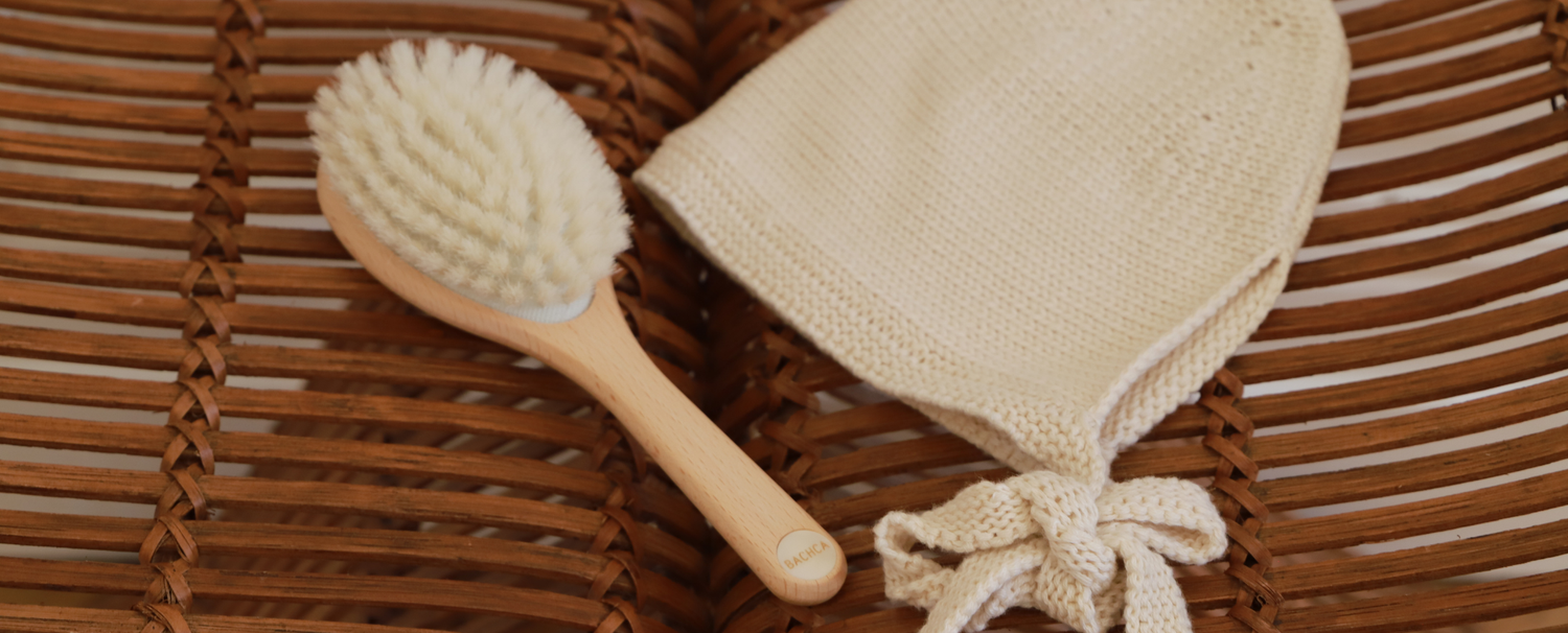 Brosse fabriquée en france en soie de chèvre de la marque Bachca posée sur une chaise en bois à côté d'un bonnet en maille beige.