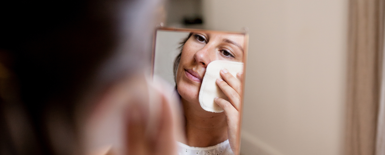 Femme tenant un miroir dans les mains se démaquillant à l'aide d'un coton réutilisable de la marque Bachca. 