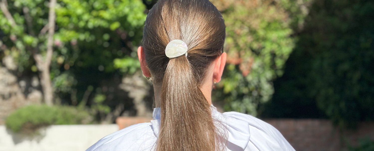 Femme de dos portant dans ses cheveux en queue de cheval l'élastique plaque nacré de la marque Bachca. 