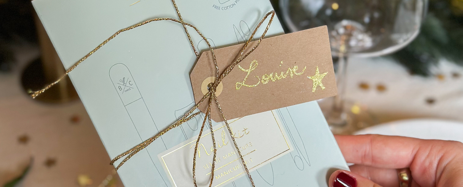 Zoom sur le kit manucure de la marque Bachca emballé d'un ruban avec une étiquette où le prénom Louise est noté. 