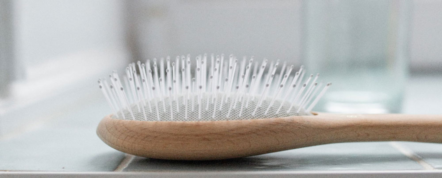 Brosse à cheveux démêlage et volume posée sur le rebord d'une baignoire. 