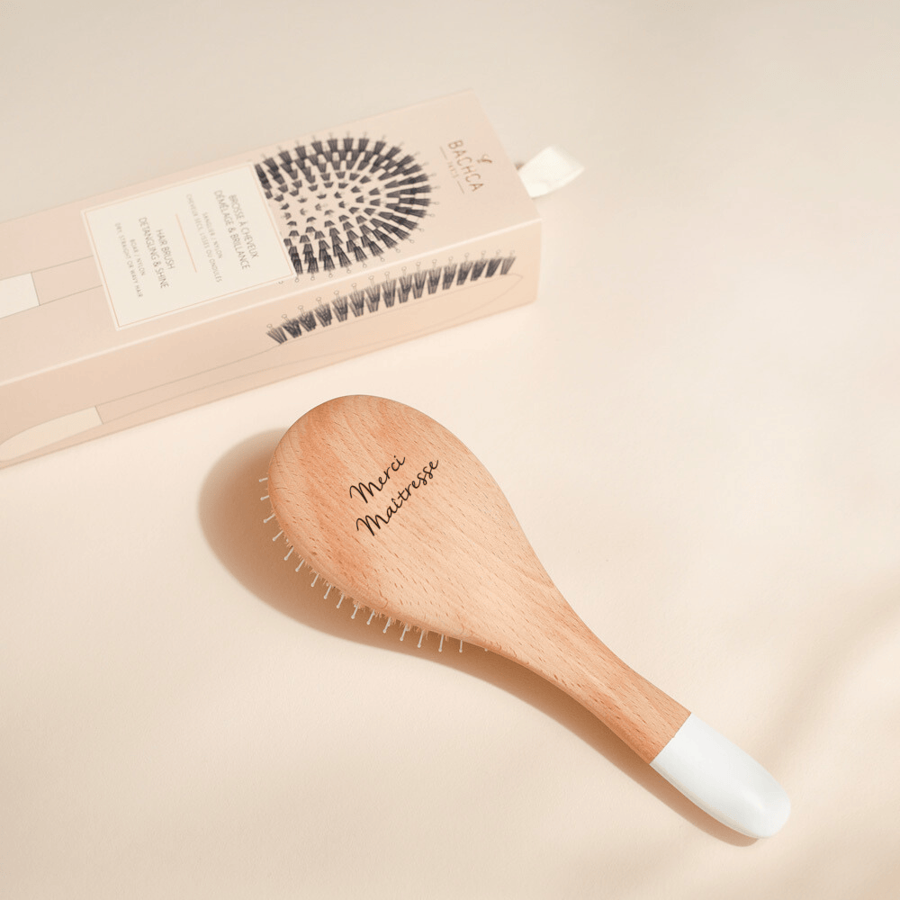 Brosse à cheveux Bachca en bois gravée "Merci Maîtresse", posée devant sa boîte illustrée.