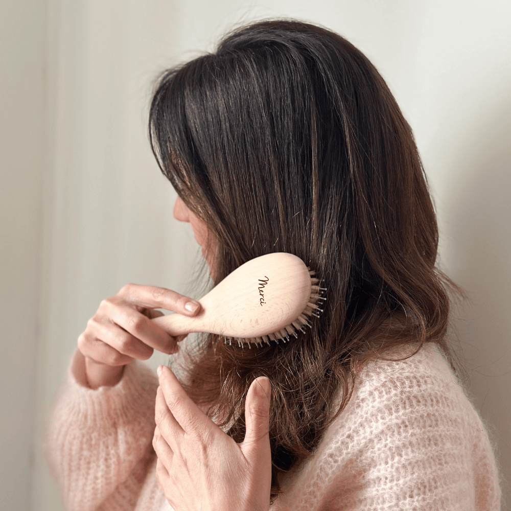 Femme se brossant les cheveux avec une brosse Bachca en bois gravée du mot &quot;Merci&quot;.