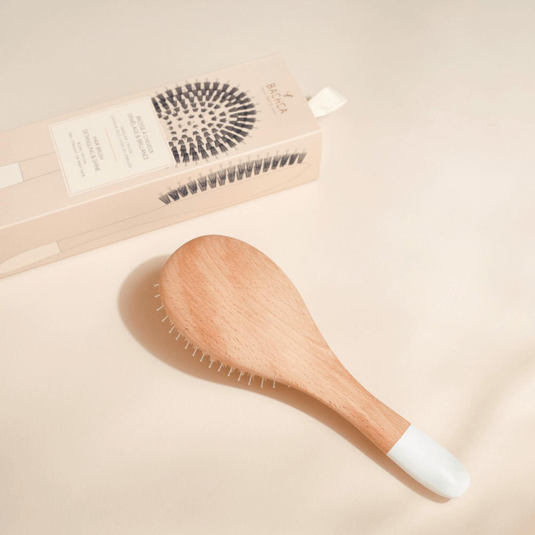 Brosse démêlante Bachca en bois de hêtre avec embout blanc, présentée à côté de son coffret d’emballage beige illustré, sur fond clair.