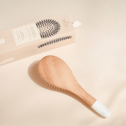 Brosse démêlante Bachca en bois de hêtre avec embout blanc, présentée à côté de son coffret d’emballage beige illustré, sur fond clair.