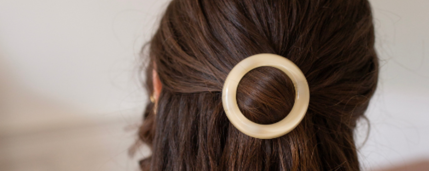 Zoom sur une barrette ronde ivoire de la marque Bachca qui tiens de beaux cheveux bruns en demi-queue.