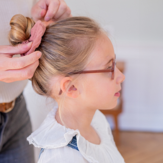 Petite fille coiffée d’un chignon haut attaché avec un chouchou en gaze de coton rose Bachca, coiffure douce et élégante.