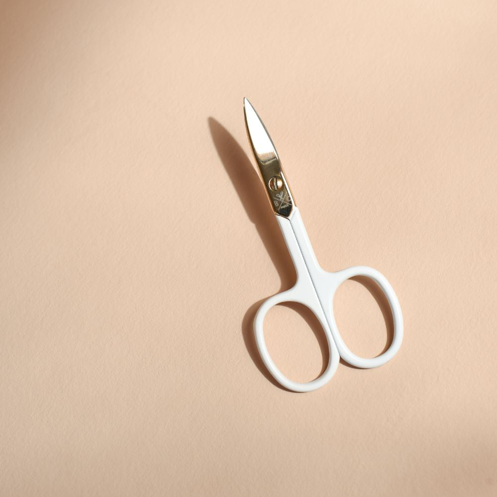 Ciseaux à ongles BACHCA au design doré et manches blancs mats, posés sur fond beige, accessoire de manucure élégant et précis pour couper les ongles avec soin.
