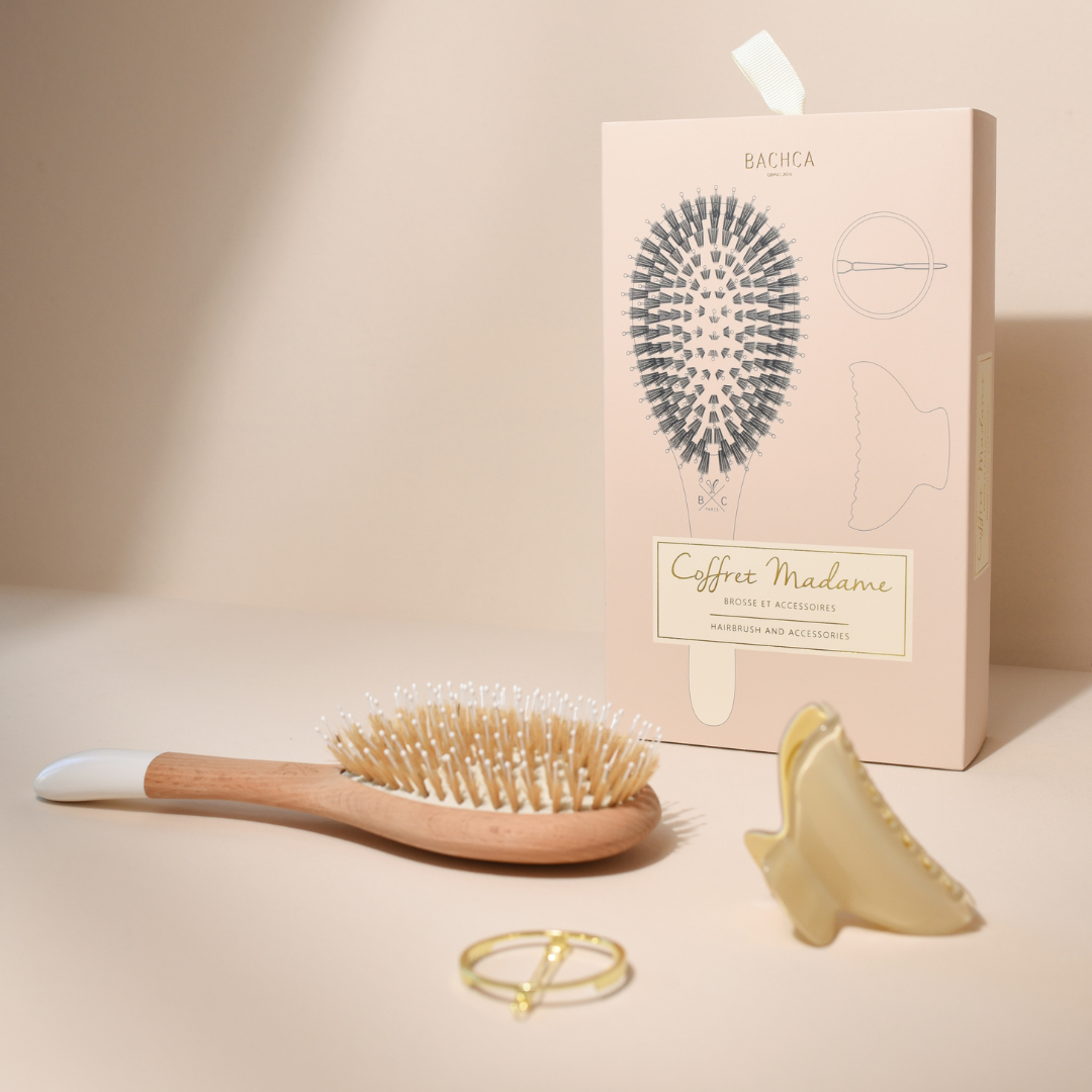 Coffret Madame Bachca avec la brosse posée devant la boîte illustrée, accompagnée d’une pince crème et d’une barrette dorée, sur fond beige doux.