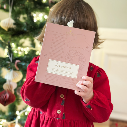 Petite fille qui tient le coffret les pépites bois de rose de la marque Bachca et cache son visage, en arrière plan on peut voir un sapin de noël.
