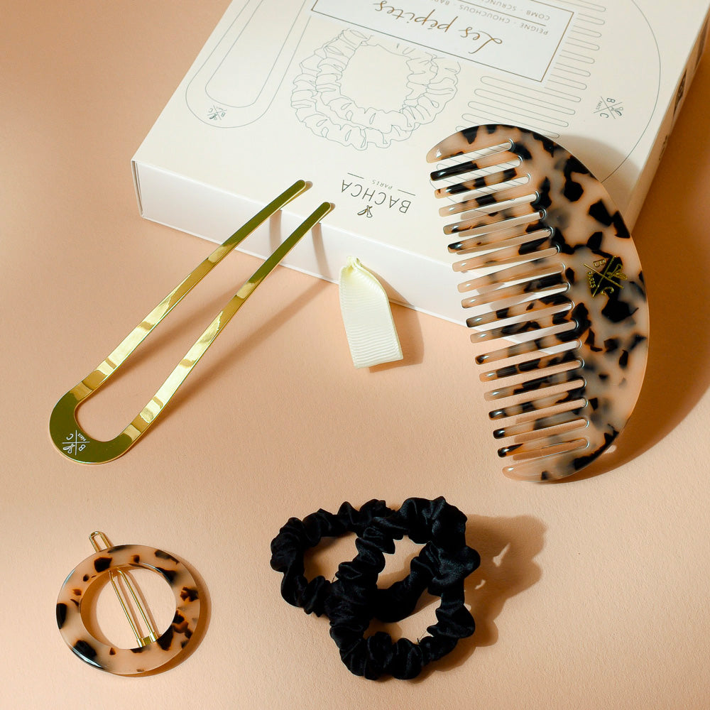 Coffret Les Pépites écaille Bachca avec peigne demi-lune en acétate, épingle à cheveux dorée, pince ronde écaille et deux chouchous noirs, élégamment disposés sur leur boîte blanche.