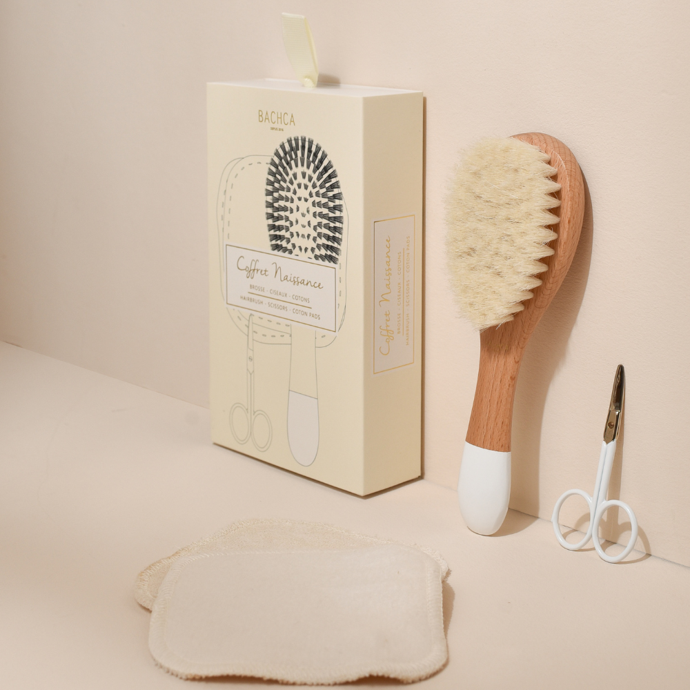 Coffret naissance Bachca, on peut voir la boîte du coffret, la brosse à cheveux nourrisson, des ciseaux bébé ainsi qu&
