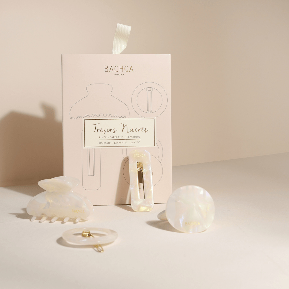 Coffret d’accessoires cheveux en nacre de la marque Bachca : pince, barrette, barrette ronde et élastique plaque, présentés sur fond rose pâle.