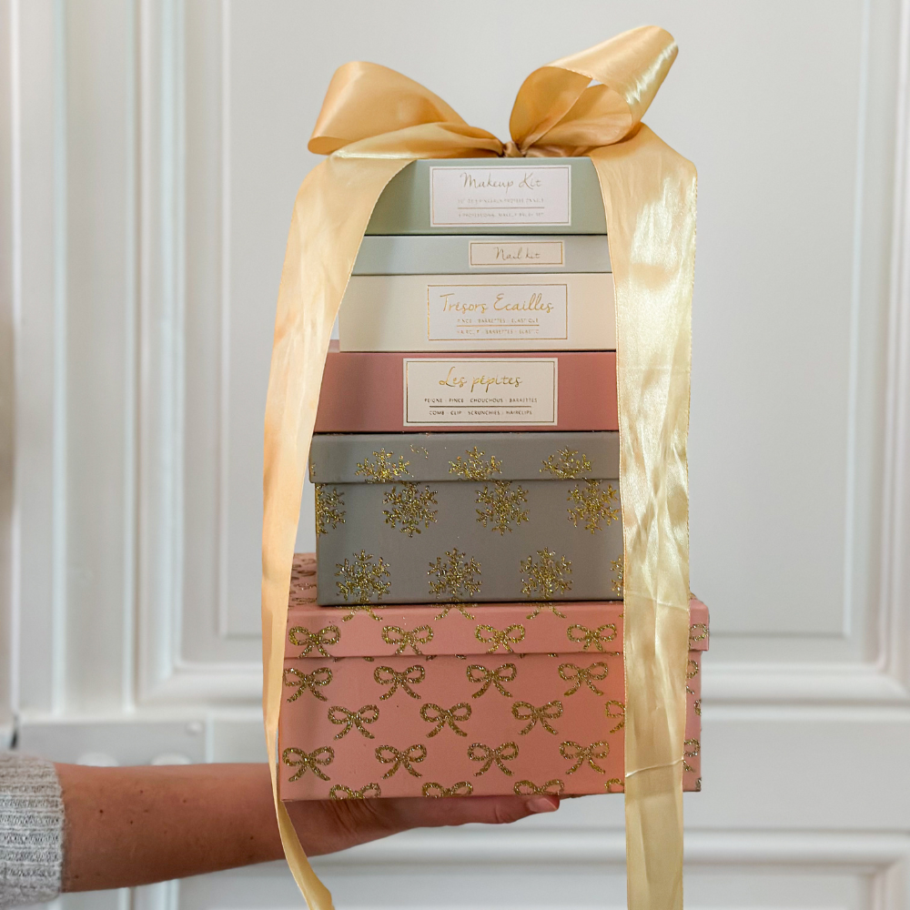 Photo de coffrets accessoires de la marque Bachca, sur un fond blanc avec moulures, un gros noeud emballe les coffrets.