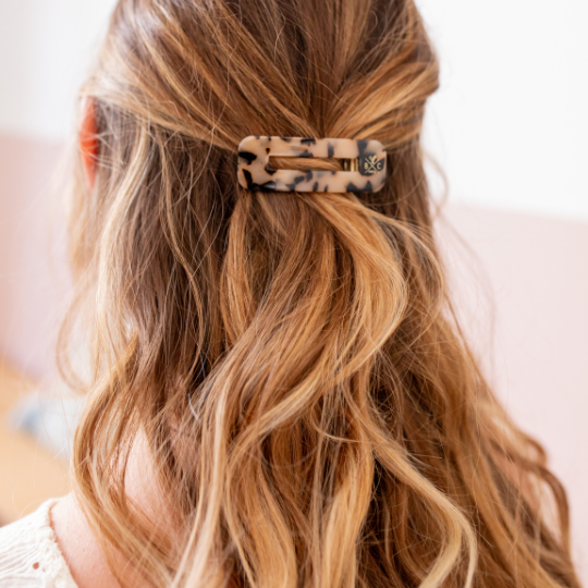 Chevelure mi-longue ondulée attachée en demi-queue avec une barrette rectangle écaille Bachca, apportant une touche élégante et graphique à la coiffure.