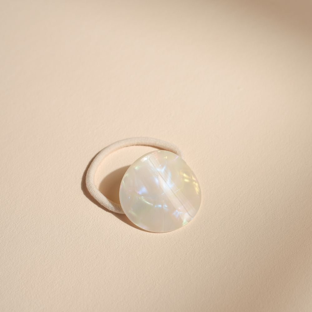 Élastique Bachca avec plaque en acétate de cellulose effet nacré, accessoire cheveux élégant et naturel photographié sur fond beige minimaliste.