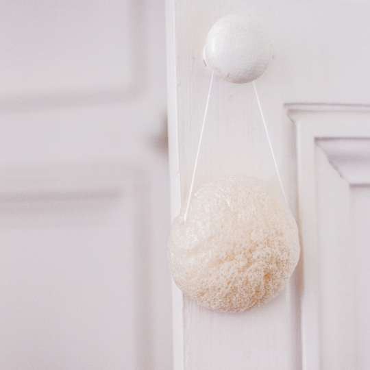 Éponge konjac naturelle Bachca suspendue à une poignée de porte, accessoire beauté pour le soin du visage.