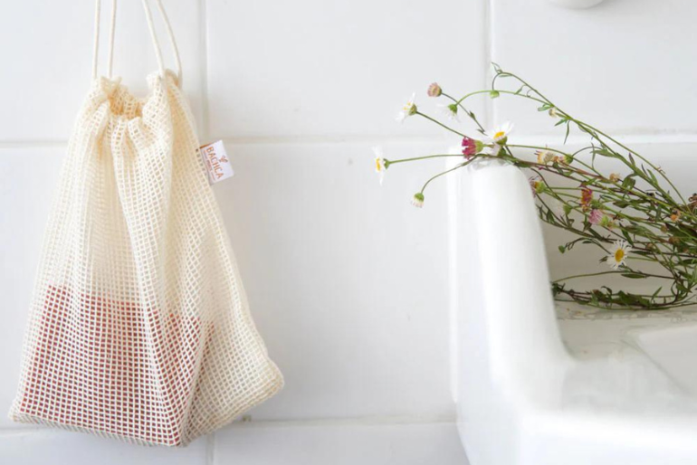ilet à savon Bachca suspendu à un crochet mural, près d’un lavabo blanc sur lequel reposent des fleurs fraîches aux tons doux.