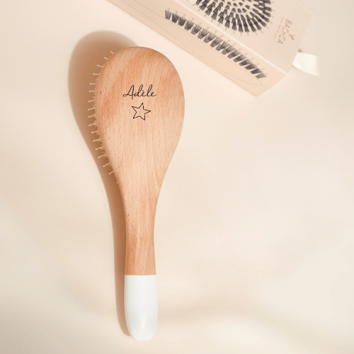 Brosse à cheveux en bois gravée au nom de Adèle avec une étoile posée sur un fond studio rose pâle.