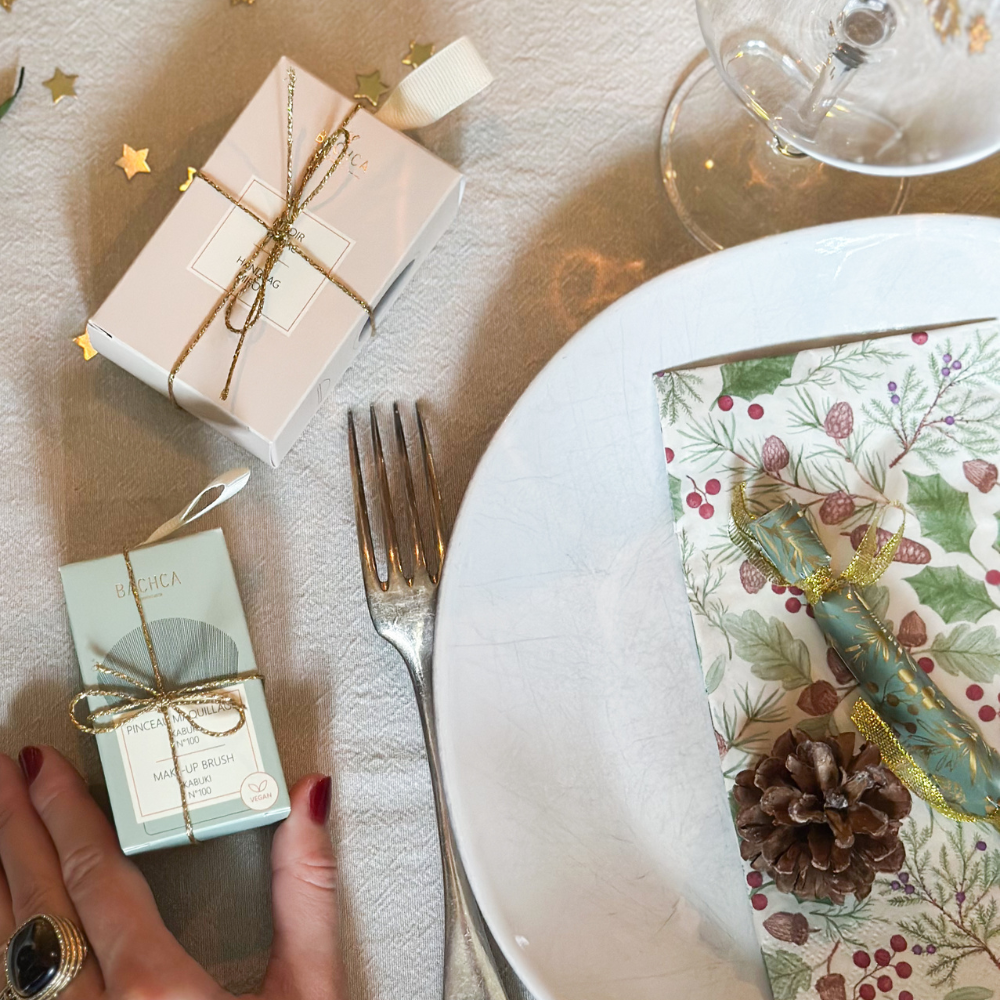 On peut apercevoir un pinceau kabuki et un miroir de poche de la marque Bachca emballés sur une table décorée pour noël.