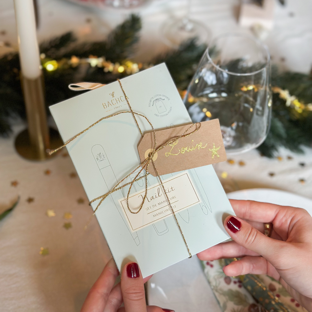 Une femme tient dans ses main le kit manucure de la marque Bachca, en fond, on peut voir une table décorée pour noël.