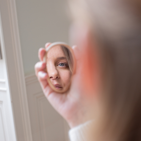 Femme tenant un miroir de poche rond Bachca et observant son reflet, accessoire beauté élégant.