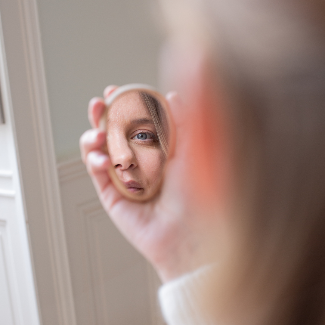 Reflet d’un visage féminin dans un petit miroir rond Bachca tenu à la main, accessoire de beauté compact et élégant.