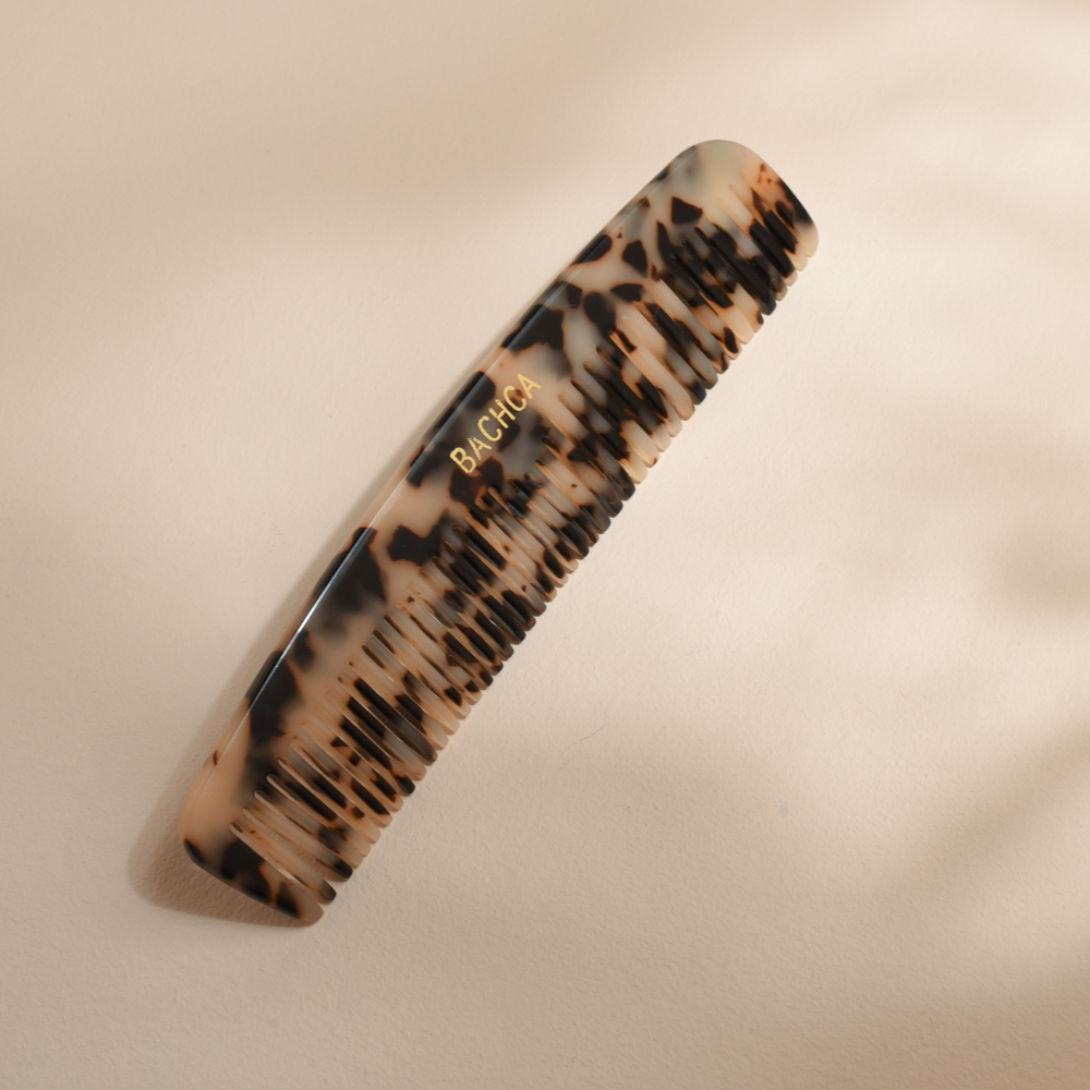 Peigne fin Bachca en acétate motif écaille posé sur une surface beige.