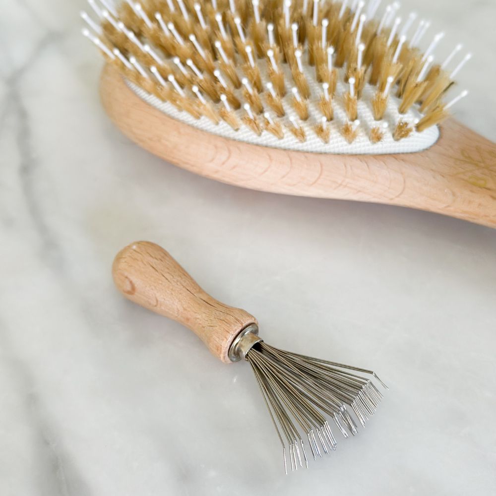 Peigne nettoyant pour brosses Bachca en bois posé sur du marbre à côté d’une brosse en poils de sanglier.