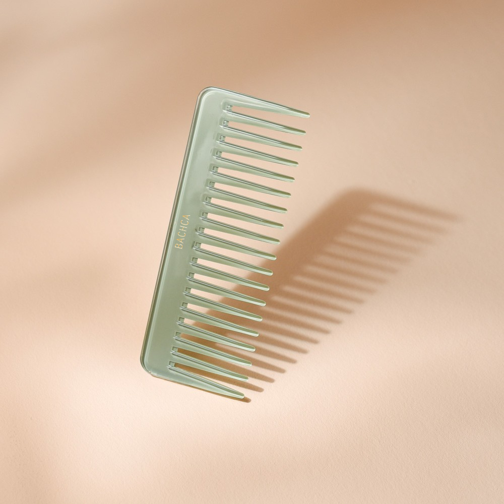 Peigne à cheveux en acétate vert d’eau aux dents larges et espacées, signé Bachca, présenté sur fond rose pâle.