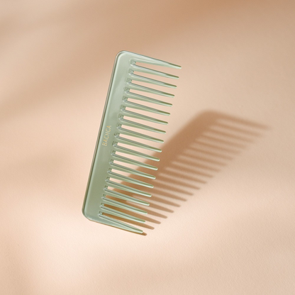 Peigne à cheveux en acétate vert d’eau aux dents larges et espacées, signé Bachca, présenté sur fond rose pâle.