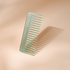 Peigne à cheveux en acétate vert d’eau aux dents larges et espacées, signé Bachca, présenté sur fond rose pâle.