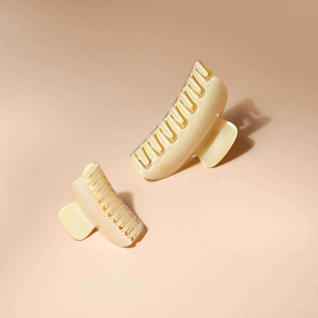 Pinces à cheveux Bachca de deux tailles en acétate effet ivoire, vues de dos, posées sur un fond beige lumineux. Le design structuré met en valeur les dents épaisses et le fini brillant des pinces.