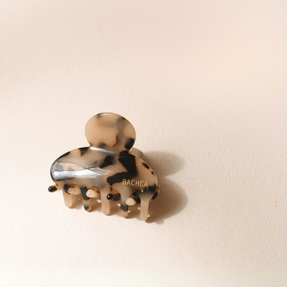 Petite pince à cheveux motif écaille de la marque Bachca, présentée sur fond rose pâle.