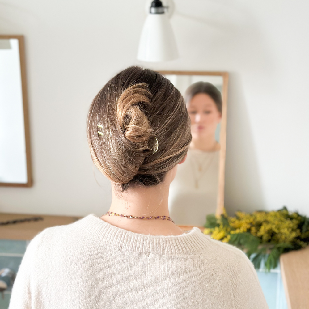 Femme de dos devant un miroir de salle de bain avec les cheveux attachés en chignon banane à l&