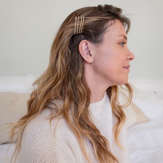 Femme aux cheveux ondulés portant trois pinces guiches dorées Bachca sur le côté pour maintenir une mèche.