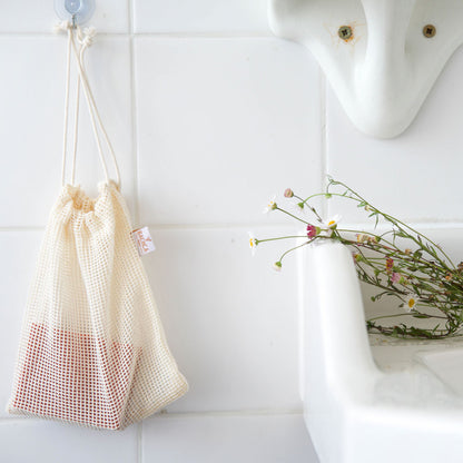 Petit sac à savon Bachca en coton filet accroché dans une salle de bain blanche, accessoire pratique et naturel.
