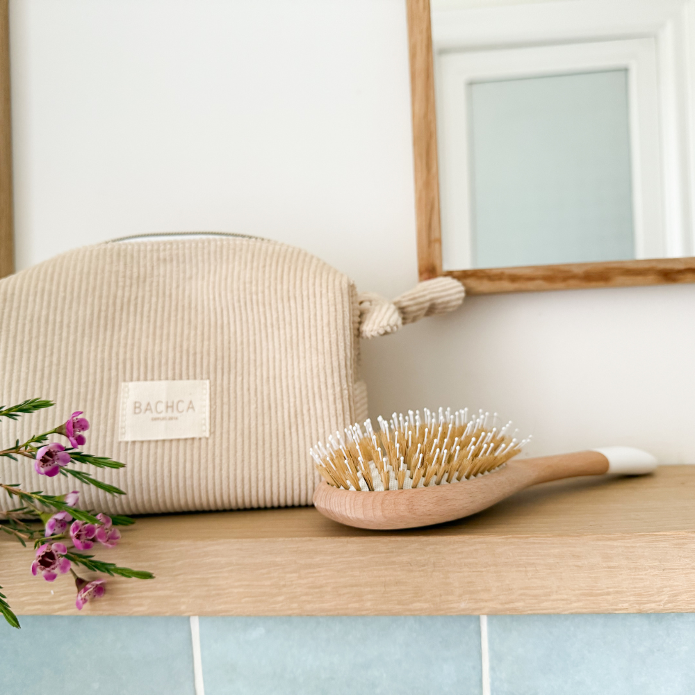 Trousse de toilette et brosse à cheveux de la marque Bachca déposés sur une étagère de salle de bain. 