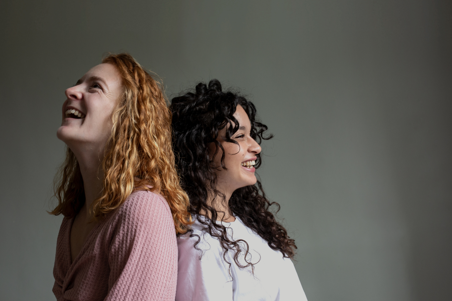 Deux jeunes femmes dos à dos souriant.