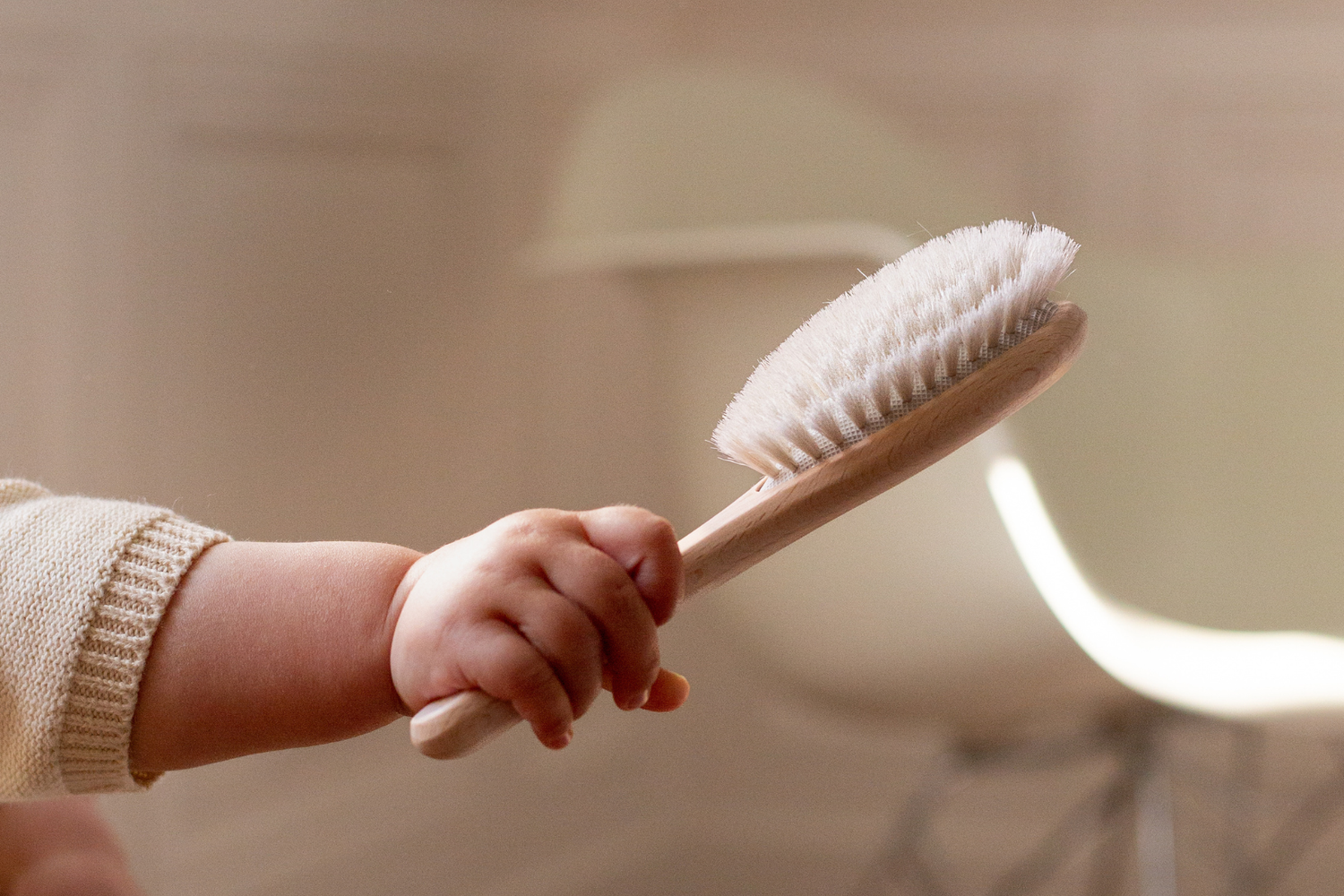 Petite main de bébé tenant une brosse à cheveux en poils de chèvre de la marque Bachca fabriquée en France.