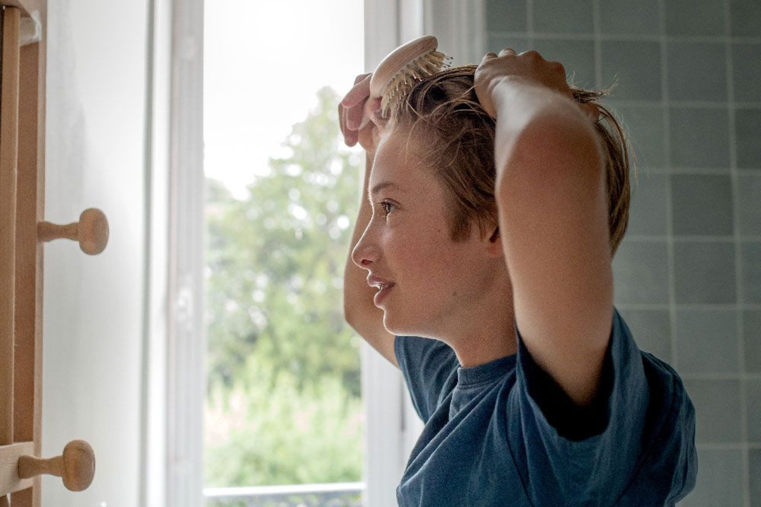 Jeune homme se de profil se brossant les cheveux devant un miroir à l'aide d'une brosse à cheveux de la marque Bachca.