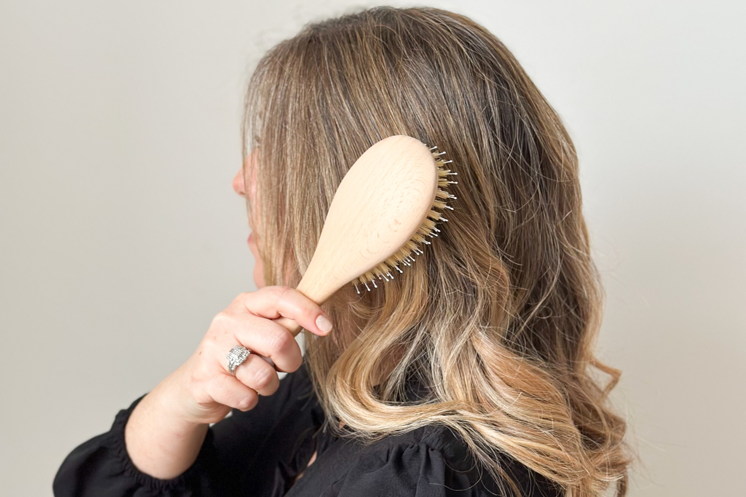 Femme blonde de profil utilisant une brosse à cheveux Bachca pour démêler ses cheveux.