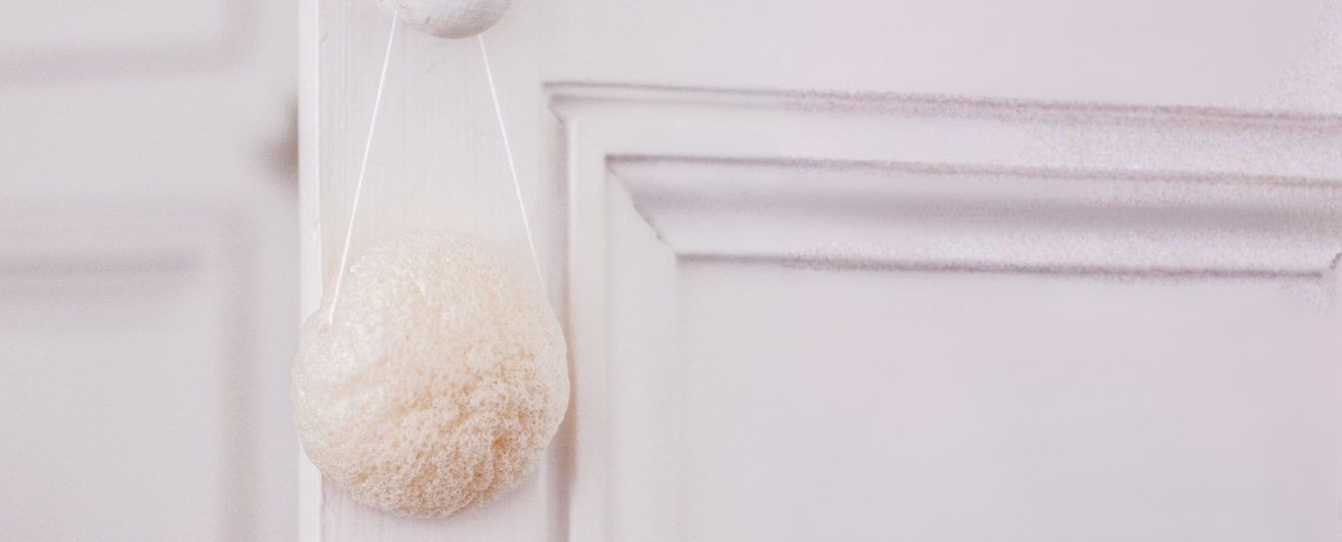 Gros plan sur l'éponge nettoyante konjac de la marque Bachca accrochée à une poignée de porte blanche.