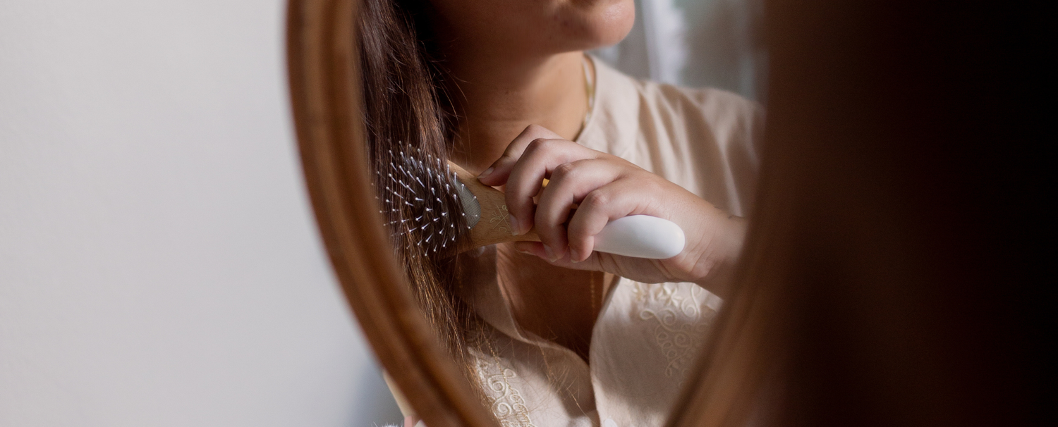 Reflet dans un miroir d'une femme aux cheveux bruns de brossant les cheveux à l'aide d'une brosse Bachca.