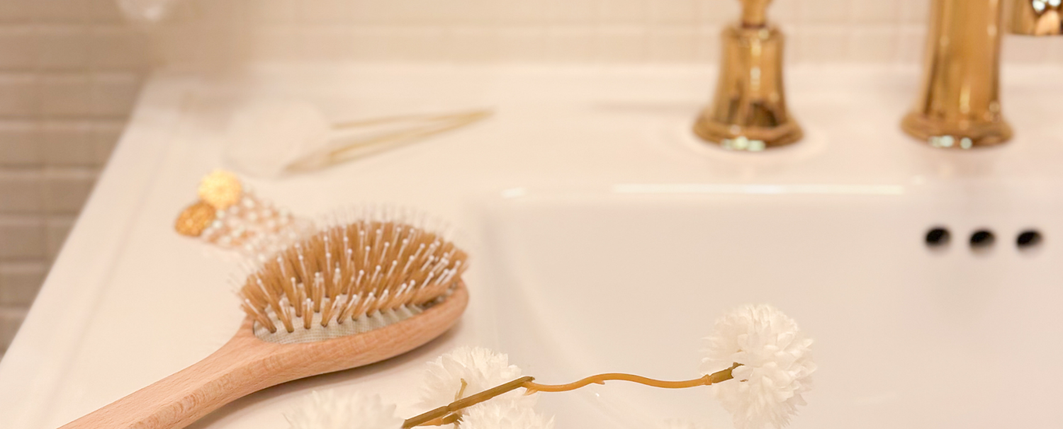 Brosse à cheveux Made in France de la marque Bachca posée sur le rebord d'un lavabo de salle de bain.