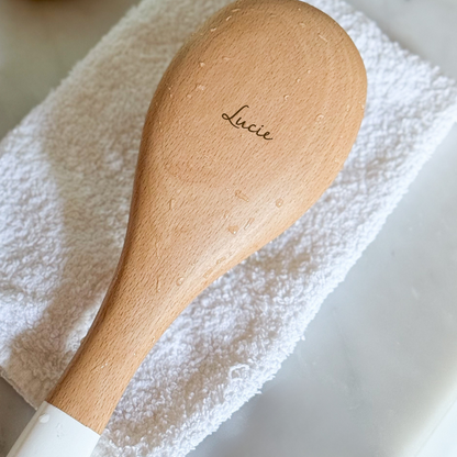Brosse à cheveux posée sur une serviette blanche avec une gravure &quot;Lucie&quot;.