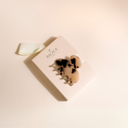 Petite pince à cheveux écaille de la marque Bachca sur fond studio rose poudré.